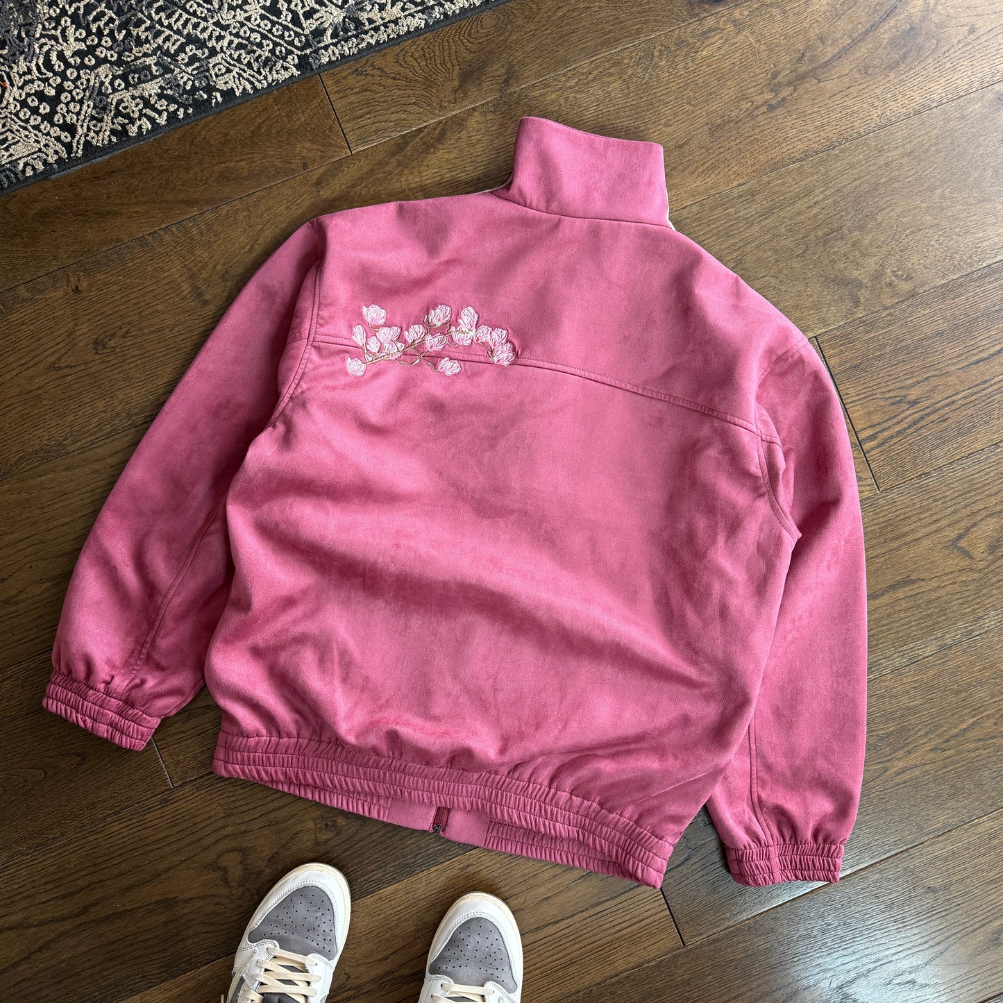 Pink sweatpants on a wooden floor with a person wearing gray sneakers.
