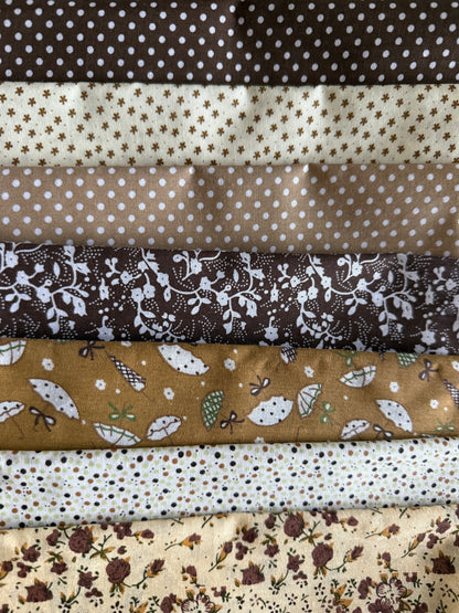 A stack of folded fabric samples with various patterns, including polka dots, floral prints, and leaf motifs in earthy brown, beige, and cream tones.