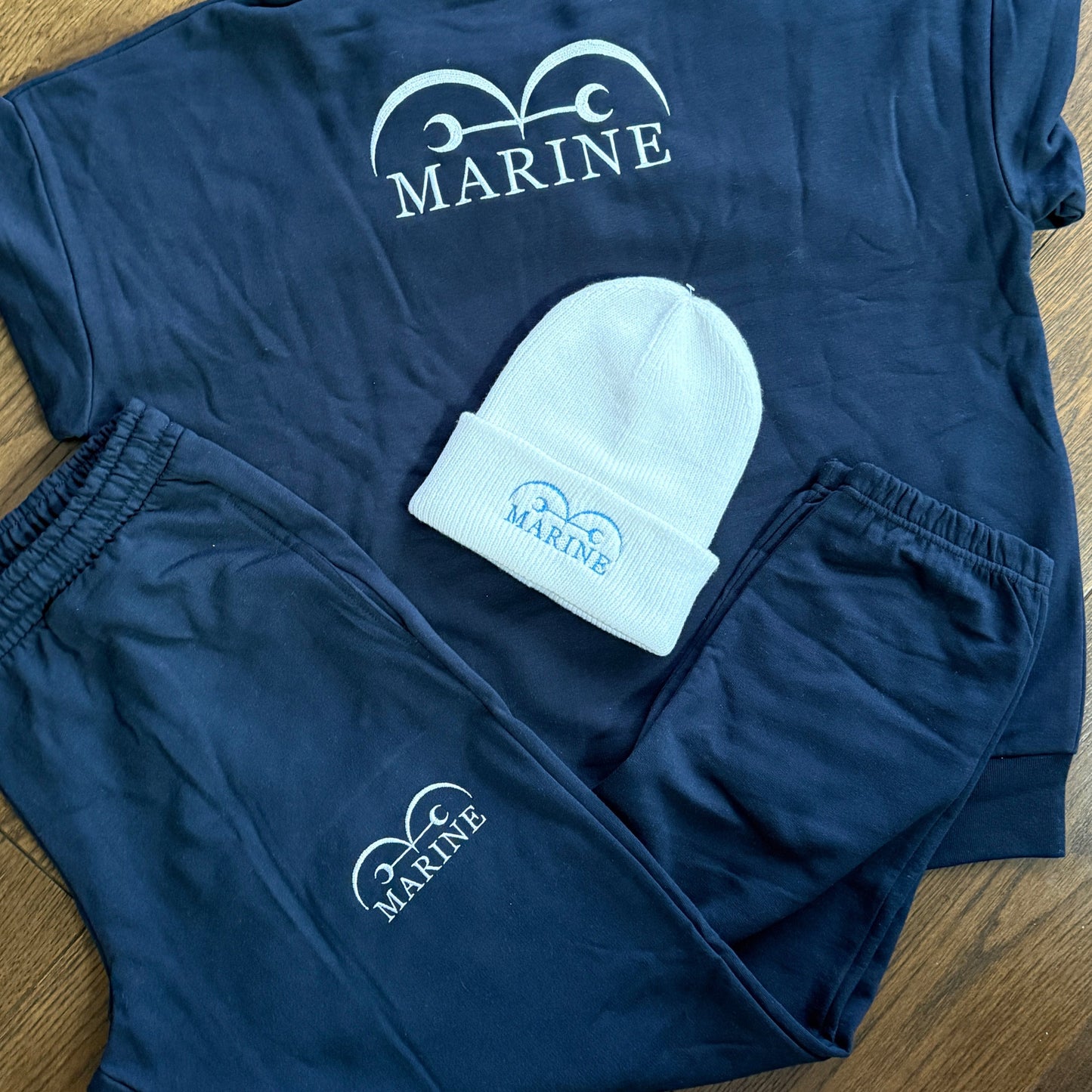Navy blue hoodie, shorts, and beanie with branding on a wooden floor.
